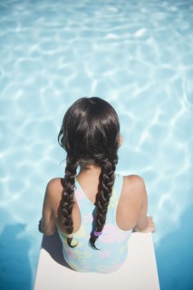Hispanic girl sitting on diving board over swimming pool