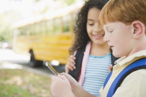 Children using cell phone while waiting for school bus