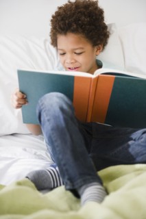 Black boy reading book in bed