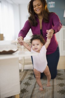 Mixed race woman helping baby learn to walk