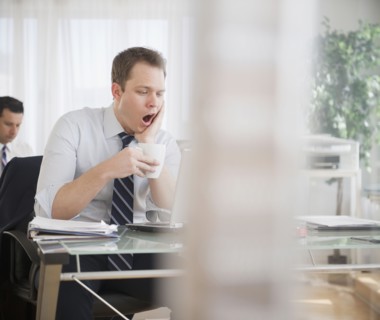 Caucasian businessman drinking coffee and yawning