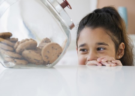 Mixed race girl looking at cookies in cookie jar