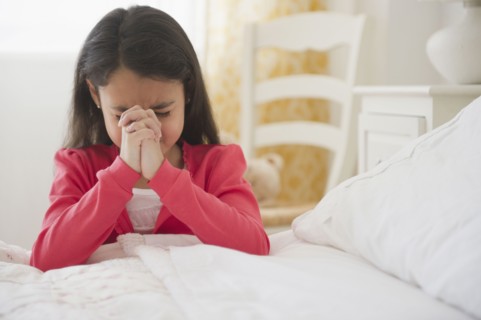 Mixed race girl praying in bedroom