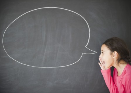 Mixed race girl standing by speech bubble on blackboard