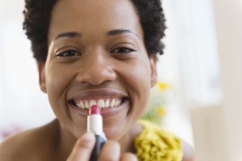 African American woman putting on lipstick