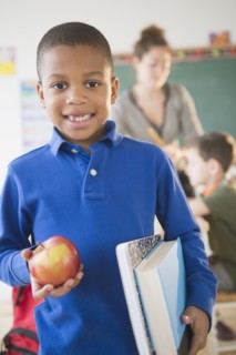 African American boy holding apple in classroom