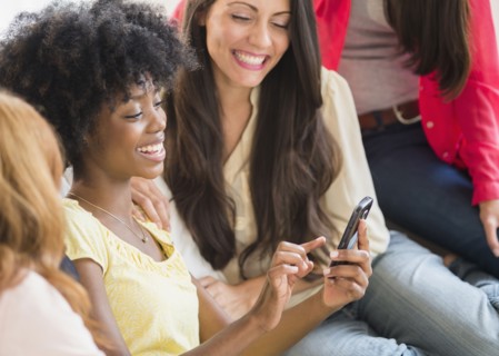 Women using cell phone together on sofa