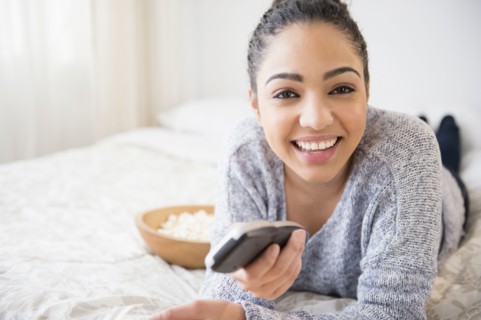 Hispanic woman watching television on bed