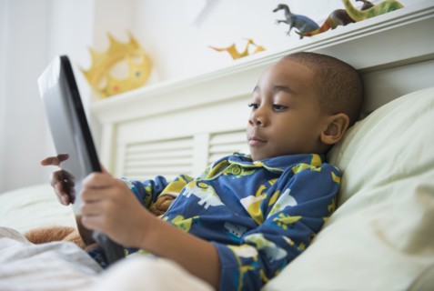 African American boy using tablet computer in bed