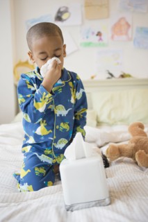 African American boy blowing his nose on bed