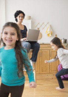 Mother using laptop as daughters play