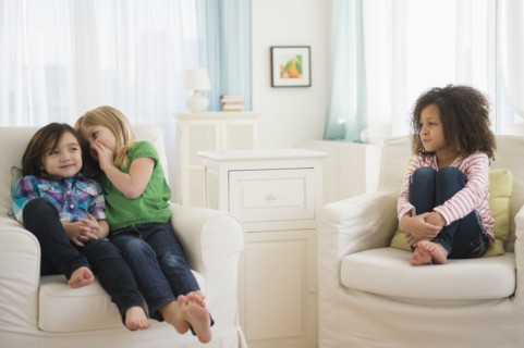Girls whispering away from friend in living room