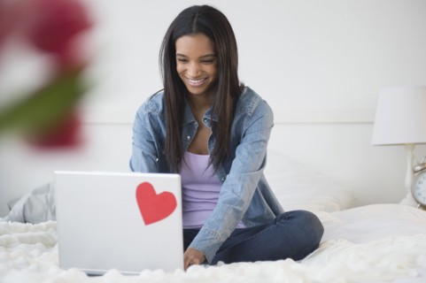 Mixed race woman using laptop on bed