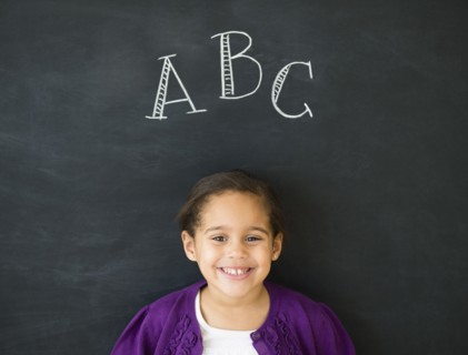 Hispanic girl standing under 'ABC' on chalkboard