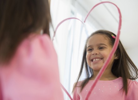 Hispanic girl making lipstick heart in mirror