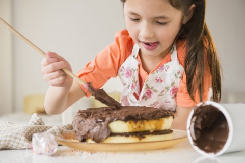 Mixed race girl icing cake in kitchen