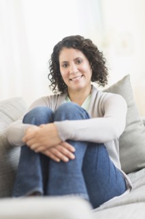 Hispanic woman hugging her knees on sofa