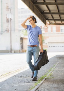 Caucasian man carrying guitar case on city street