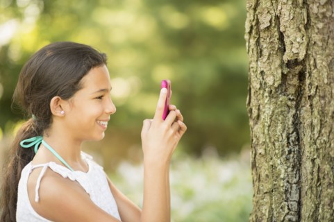 Mixed race girl photographing tree trunk with camera phone