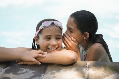 Mixed race girls whispering in swimming pool