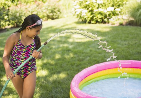 Mixed race girl filling wading pool in backyard