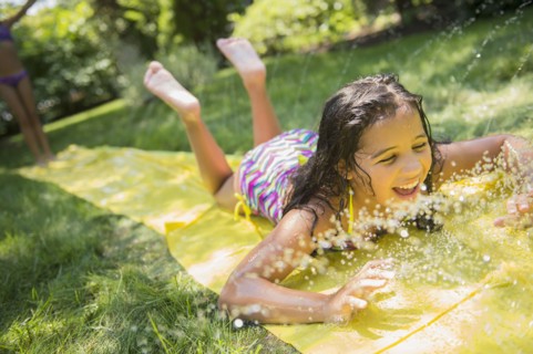 Mixed race girls playing on slip and slide in backyard