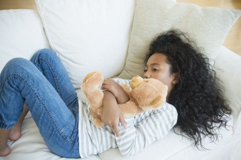 Mixed race girl hugging teddy bear on sofa