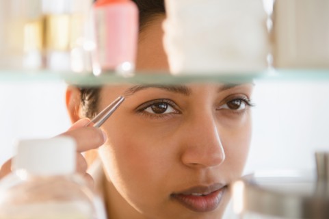 Close up of Asian woman tweezing eyebrows