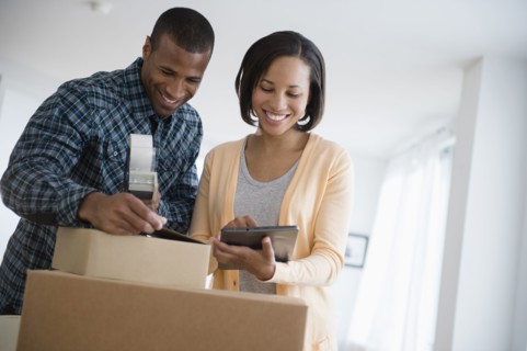 Couple with digital tablet taping up moving boxes