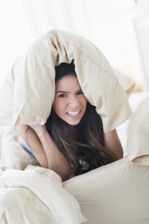 Portrait of frustrated Hispanic woman under pillow in bed