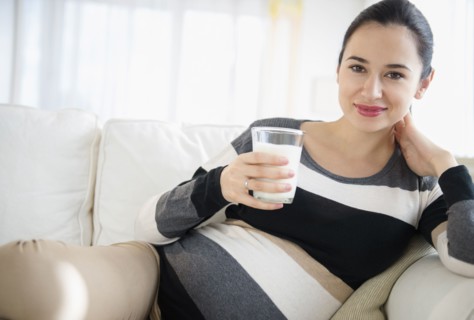 Pregnant Caucasian woman drinking milk on sofa