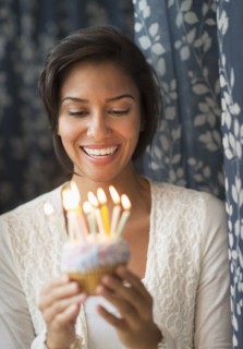Hispanic woman looking down at lit candles on birthday cupcake