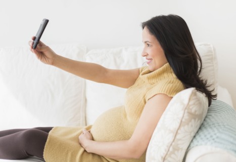 Pregnant Hispanic woman taking picture with cell phone