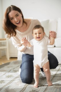 Mother helping baby stand in living room