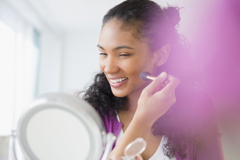 Mixed race woman applying makeup in mirror