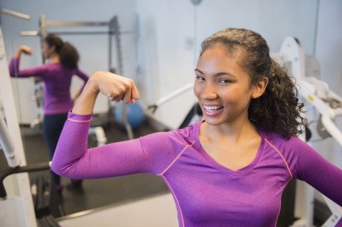 Mixed race woman flexing muscles in gym