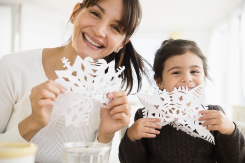 Hispanic mother and daughter making paper snowflakes