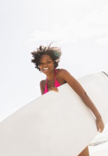 African American woman carrying surfboard on beach