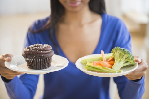 Mixed race woman choosing vegetables or cupcake