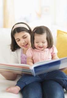 Hispanic girl reading to toddler sister in living room