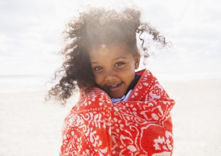 Mixed race girl wrapped in towel on beach