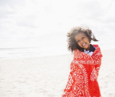 Mixed race girl wrapped in towel on beach