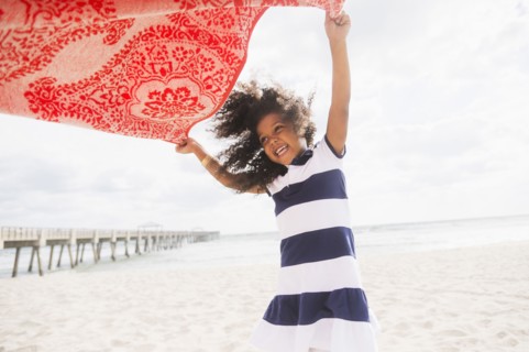 Mixed race girl playing with towel on beach
