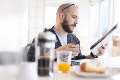 Hispanic man reading newspaper at breakfast