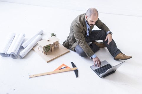 Hispanic architect using laptop on floor
