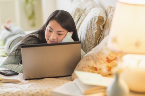 Mixed race teenage girl doing homework on bed