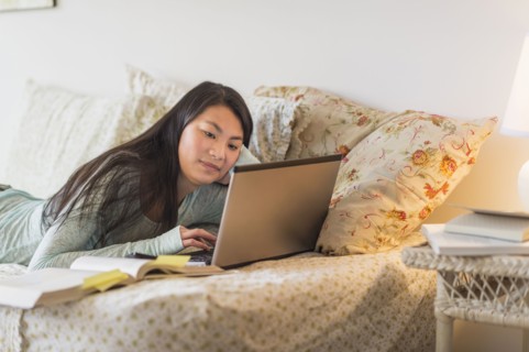Mixed race teenage girl doing homework on bed