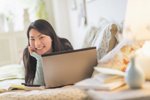 Mixed race teenage girl doing homework on bed