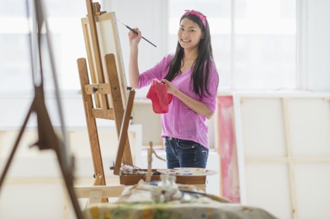 Mixed race teenage girl painting in studio