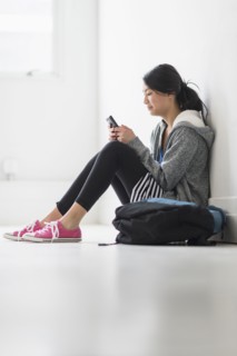 Mixed race teenage girl using cell phone in school hallway